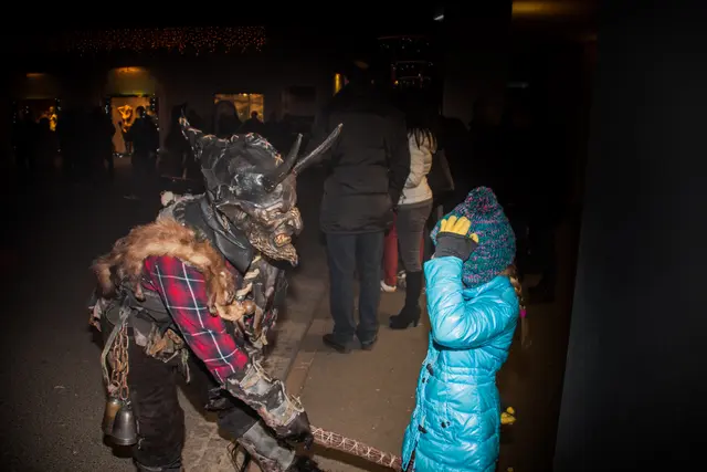 Gruseliger Krampus richtet die Rute auf ein Mädchen. 
