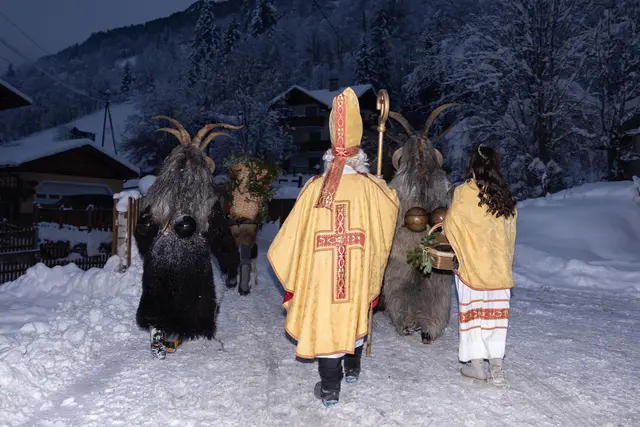 Nikolaus und Krampus stapfen in der Dämmerung von Haus zu Haus. 