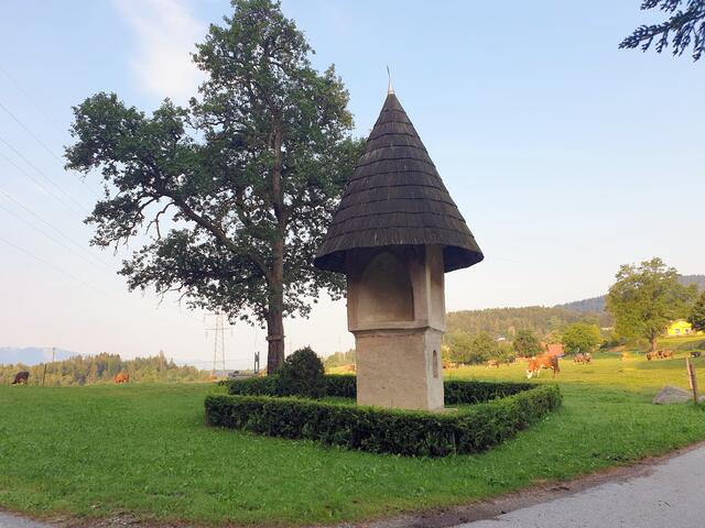 Das Tschachonigkreuz ist ein um 1500 errichteter spätgotischer Nischenbildstock mit einem verschindelten Kegeldach. Seine Höhe von 8 Meter macht ihn zum größten Kärntner Bildstock aus dieser Epoche. Das Hauptgeschoß ist tabernakelartig und öffnet sich in vier gewölbten Spitzbogennischen. Neben den fast vollständig erhaltenen spätgotischen Putzen sind noch spätgotische Wandmalereireste sichtbar. Die Fresken wurden 1908 restauriert. Die südseitige Nische zeigt den hl. Martin zu Pferd, sowie im Gewölbe den Markuslöwen und eine Monstranz. In den Zwickeln wird die Verkündigung Mariä dargestellt. Die ostseitige Nische zeigt einen Wundmalchristus und darüber einen Matthäusengel sowie das Schweißtuch Christi. Außen sind die hll. Barbara sowie der Erasmus sichtbar. Rechts unten befinden sich gotische initialartige Zeichen. Die nordseitige Nische zeigt eine Kreuzigungsgruppe mit Maria und dem hl. Apostel Johannes. Im Gewölbe ist der Johannesadler sichtbar. In den Zwickeln sind zwei Heilige dargestellt. In der westlichen Nische ist Maria mit dem Kind abgebildet und darüber der Lukasstier. Außen wird ein heiliger Bischof sowie der hl. Wolfgang dargestellt.