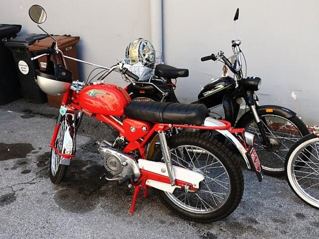 Vor der Stangl-Puch steht ein Star meiner Jugendtage. „Die MC“ hatte zwei wesentliche Erscheinungsformen. Einerseits war das Kürzel MC für Moto Cross keine Übertreibung. Eine modifizierte MC war durchaus für im Motorsport einsetzbar. Andrerseits war sie eine beliebte Basis für eine Variation a la „Captain America“ aus dem Film Easy Rider. Vorne Chrom-Zeugs und ein hoher Lenker (Apehanger), der Tank mit Stars and Stripes dekoriert, hinten ein möglichst fetter Reifen und eine Chrom-Lehne (Sissy Bar). Außerdem konnte man den Motor gut optimieren, was natürlich illegal war.