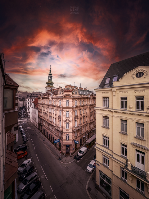 Das Bild zeigt den Kirchturm der Paulanerkirche in Wien, der sich vor einem dramatischen Abendhimmel erhebt. Die Wolkenformationen, vom letzten Licht der untergehenden Sonne in ein tiefes Rot getaucht, wirken fast bedrohlich und zugleich erhaben. Ein Symbol der Beständigkeit, der Kirchturm ragt empor, als wolle er den Himmel berühren. Doch der Anblick lädt auch zu Fragen ein: Wie wichtig ist uns heute noch unsere Kommunikation mit Gott?

Früher waren die Kirchenglocken ein unmissverständlicher Ruf zur Besinnung, ein Zeichen dafür, dass es Zeit für ein Gebet war. Sie erinnerten uns daran, innezuhalten, das Kreuzzeichen zu machen und in einem kurzen Moment des Gebets mit Gott in Verbindung zu treten. Doch was bedeuten diese Glocken heute für uns? Sind sie noch der Ruf zur Andacht oder nur der schlichte Hinweis darauf, dass eine weitere Stunde vergangen ist?

Im hektischen Alltag, in dem wir oft von Termin zu Termin eilen und von digitalen Benachrichtigungen überschwemmt werden, scheint das Bedürfnis nach Stille, nach innerer Einkehr und der Verbindung zu Gott zu schwinden. Fühlen wir noch den Drang, im Gebet Zuflucht zu suchen, um in unseren Entscheidungen, Handlungen und Begegnungen mit anderen Menschen Gottes Gegenwart zu spüren? Oder ist das nur noch eine Tradition, die in den Hintergrund gerückt ist, während wir unser Leben immer mehr selbstbestimmt und unabhängig gestalten?

Vielleicht erinnern uns die dramatischen Wolken am Himmel, in ihrer wilden Schönheit und Unvorhersehbarkeit, daran, dass es Dinge gibt, die außerhalb unserer Kontrolle liegen. Dinge, die uns dazu auffordern, innezuhalten, still zu werden und das Gespräch mit etwas Größerem als uns selbst zu suchen. Der Kirchturm bleibt dabei ein stummer Zeuge, eine ständige Einladung, Gott wieder Platz in unserem Leben zu geben – wenn wir bereit sind, zu lauschen.