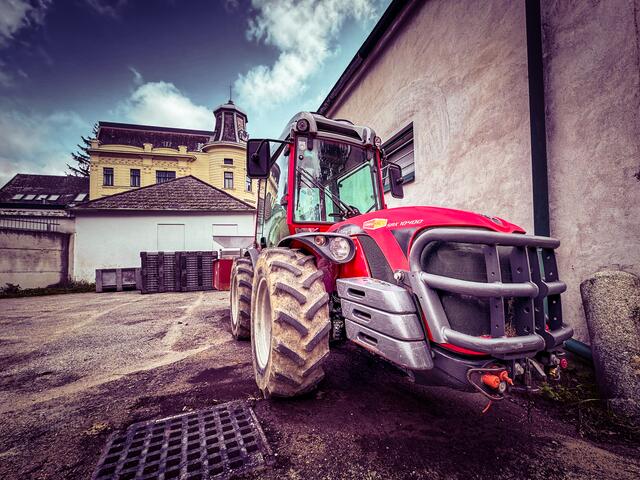 Auf dem Foto sieht man einen modernen roten Traktor, der speziell für den Einsatz in Weinbergen entwickelt wurde. Seine kompakte Bauweise und schmale Spurbreite ermöglichen es ihm, mühelos zwischen den eng gesetzten Rebzeilen zu manövrieren.