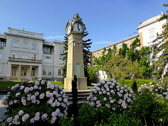 Die große Uhr auf dem Otto Wagner Areal  in Wien-Penzing ist ein historisches Detail im Jugendstil, das seit den frühen 1900er-Jahren zum Ensemble gehört. Als Teil der funktionalen Architektur des ehemaligen Steinhof-Spitals unterstreicht sie das gestalterische Gesamtkonzept von Otto Wagner auf der Baumgartner Höhe🕔