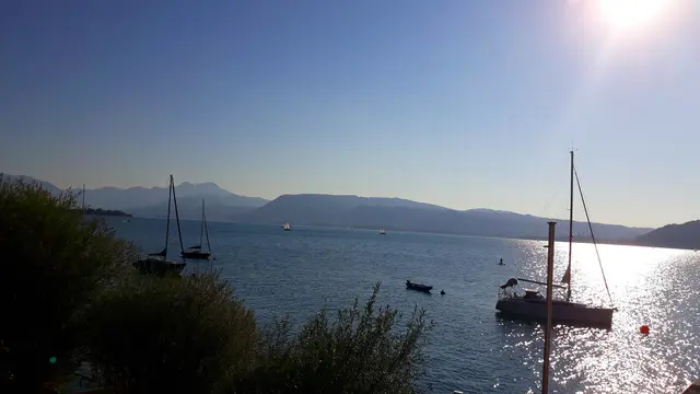 Eine Abendstimmung am See. Boote. Die Sonne beleuchtet das Wasser. Im Hintergrund: Berge und wolkenloser Himmel.