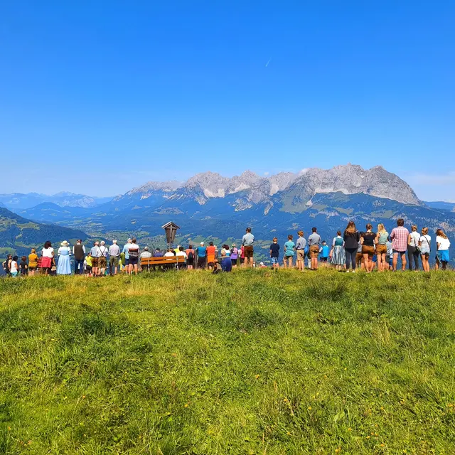 Personen nehmen an der Bergmesse bei der Stanglalm vor der Kulisse des Wilden Kaisers teil.